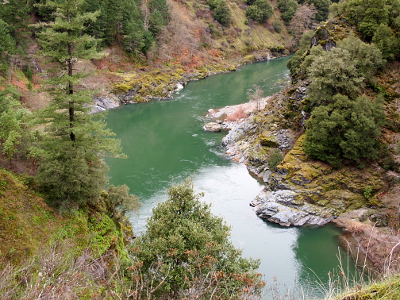 [Closeup view of a 90 degree bend in the river flow in the valley with rocks on the edges and trees growing out of the hillsides.]